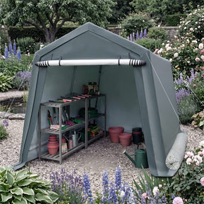 A large outdoor garden shed tent in a muted sage green color, set up in a landscaped garden with gravel flooring and gardening tools stored inside.